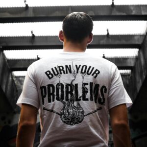 Man standing indoors, wearing a t-shirt with 'Burn Your Problems' text, viewed from behind.